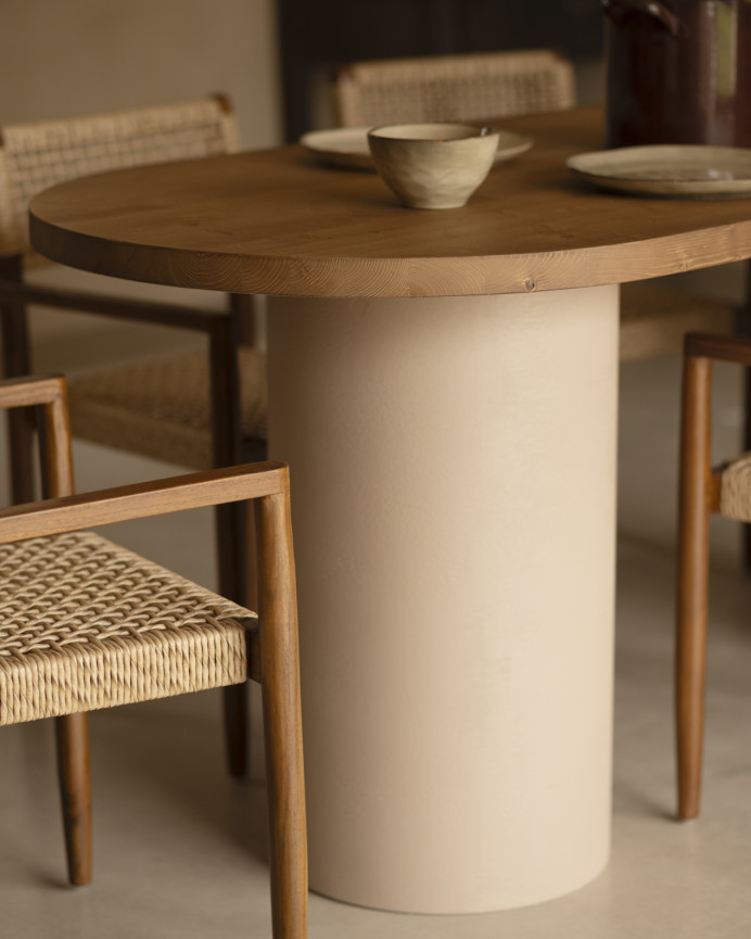 Oval dining table made of solid wood in a dark oak tone and micro cement legs in an earth tone, available in various sizes.