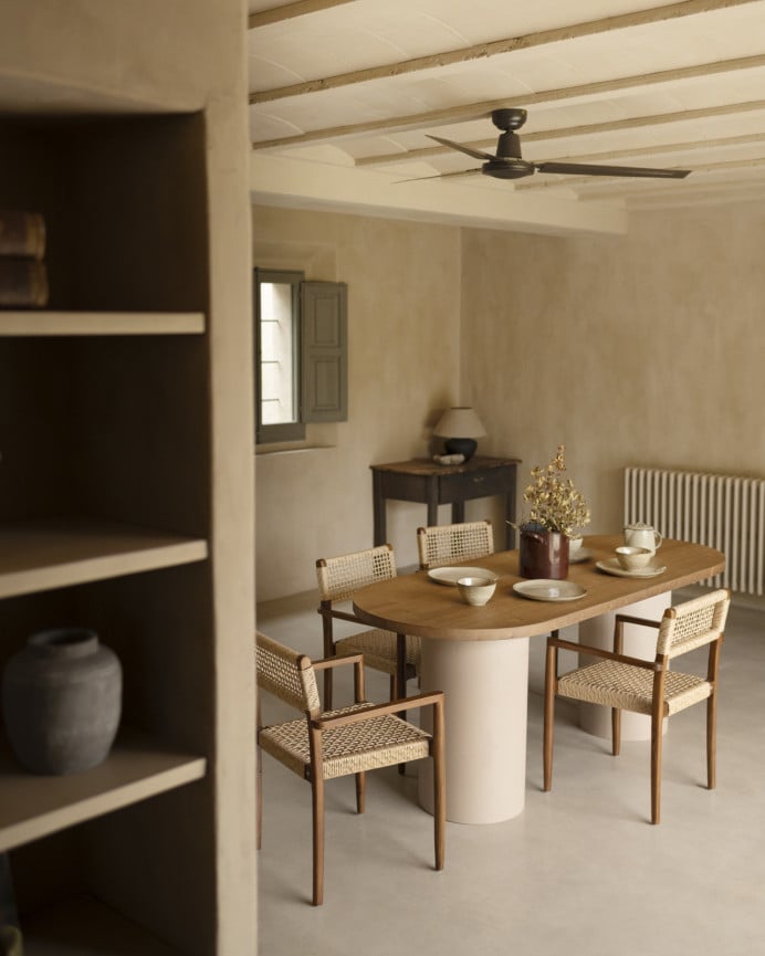 Oval dining table made of solid wood in a dark oak tone and micro cement legs in an earth tone, available in various sizes.
