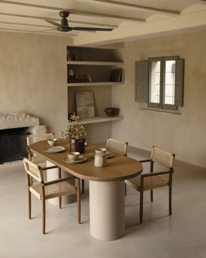 Oval dining table made of solid wood in a dark oak tone and micro cement legs in an earth tone, available in various sizes.