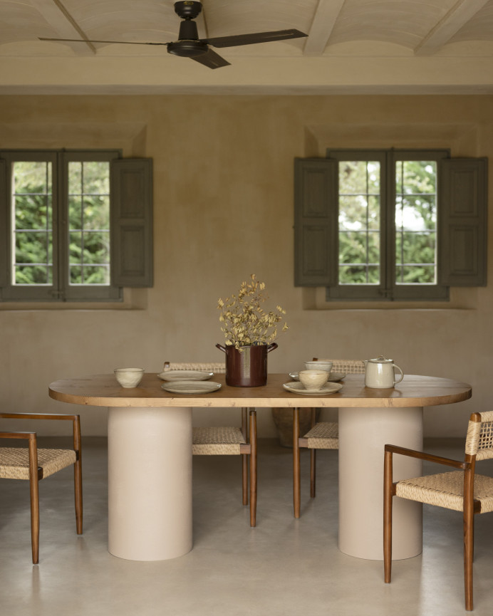 Oval dining table made of solid wood in a dark oak tone and micro cement legs in an earth tone, available in various sizes.