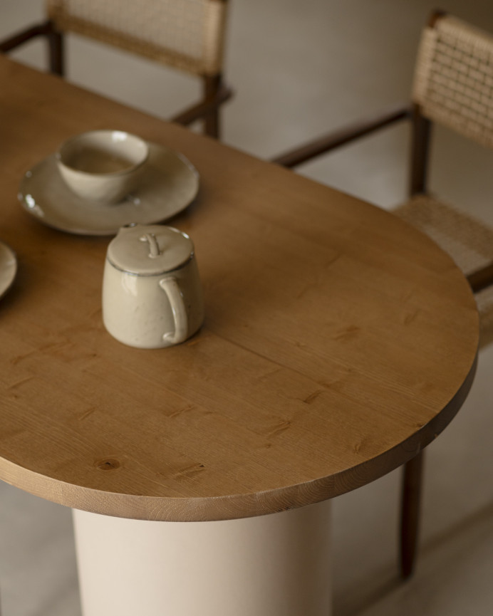 Oval dining table made of solid wood in a dark oak tone and micro cement legs in an earth tone, available in various sizes.