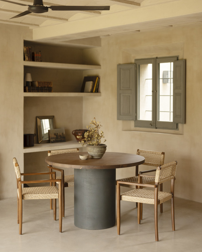 Round solid wood dining table in a dark oak tone with microcement legs in a green tone, available in various sizes.