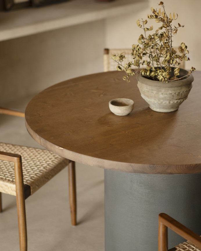 Round solid wood dining table in a dark oak tone with microcement legs in a green tone, available in various sizes.
