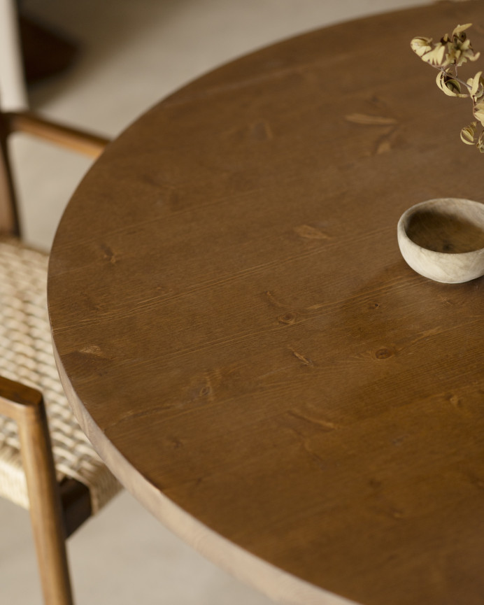 Round solid wood dining table in a dark oak tone with microcement legs in a green tone, available in various sizes.