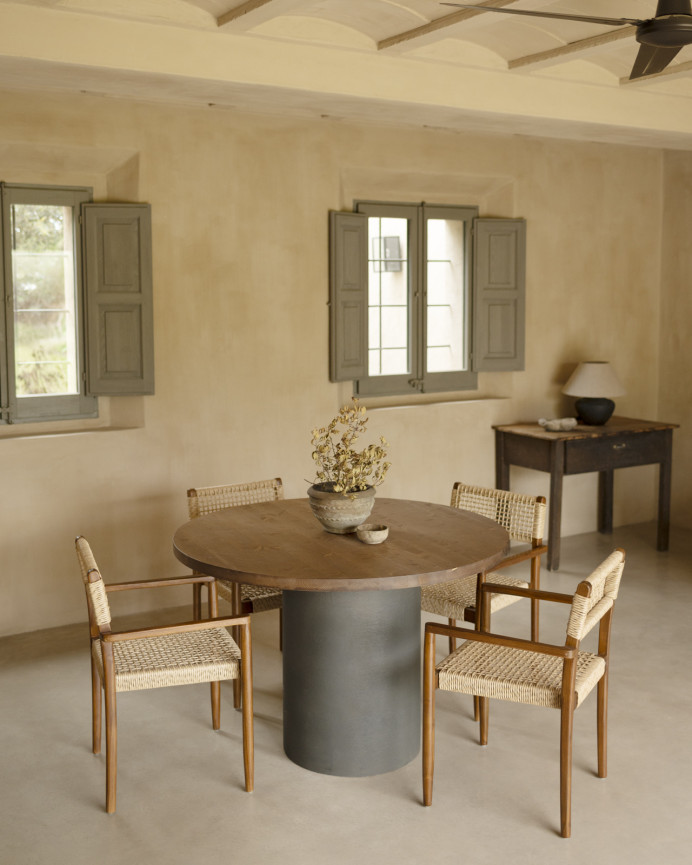 Round solid wood dining table in a dark oak tone with microcement legs in a green tone, available in various sizes.