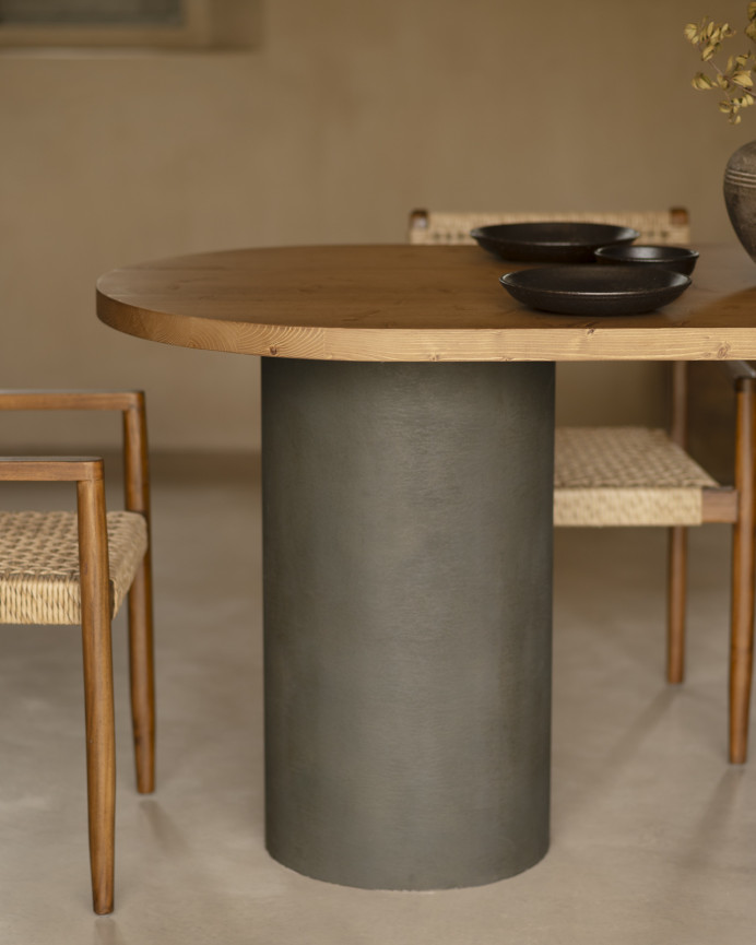 Oval solid wood dining table in dark oak tone with microcement legs in green tone, available in various sizes.