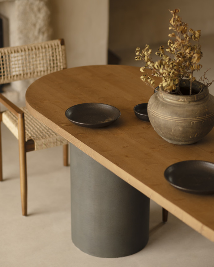 Oval solid wood dining table in dark oak tone with microcement legs in green tone, available in various sizes.