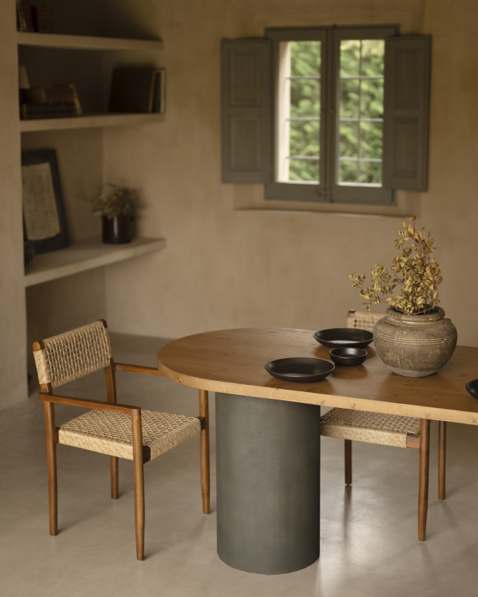 Oval solid wood dining table in dark oak tone with microcement legs in green tone, available in various sizes.