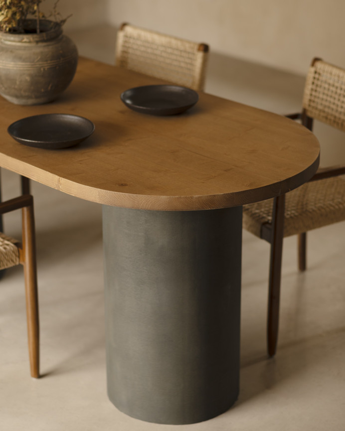Oval solid wood dining table in dark oak tone with microcement legs in green tone, available in various sizes.