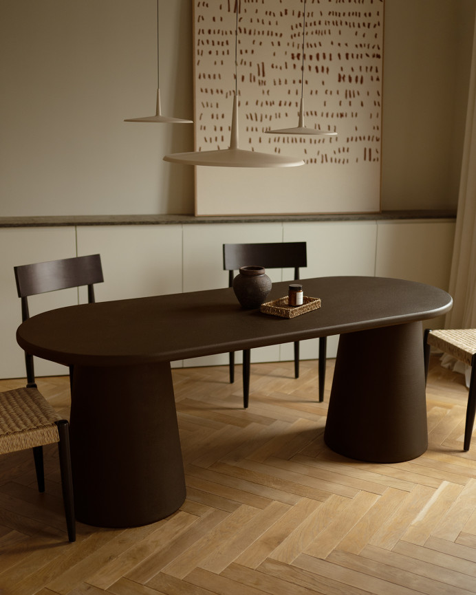 Oval dining table made of brown microcement in several sizes.