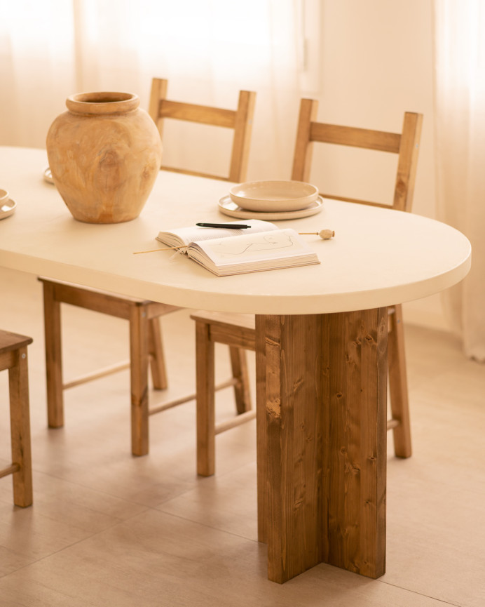 Oval dining table made of microcement in a light off-white tone with dark oak wood legs of various sizes.