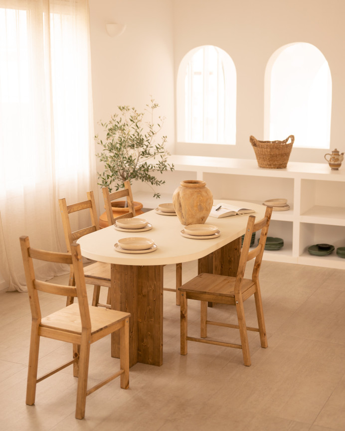 Oval dining table made of microcement in a light off-white tone with dark oak wood legs of various sizes.