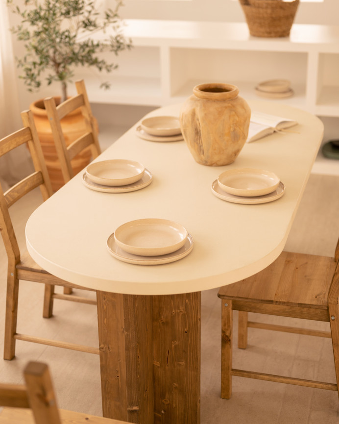 Oval dining table made of microcement in a light off-white tone with dark oak wood legs of various sizes.