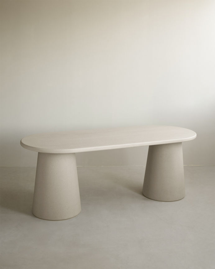 Oval dining table made of beige microcement in various sizes.