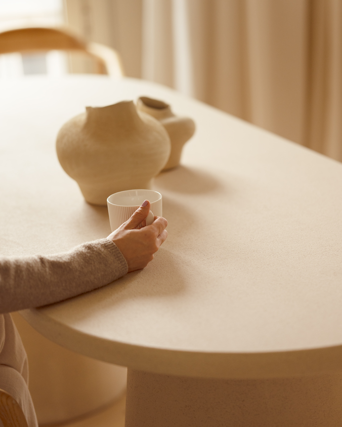 Oval dining table made of beige microcement in various sizes.