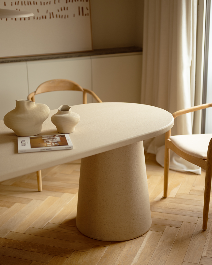 Oval dining table made of beige microcement in various sizes.