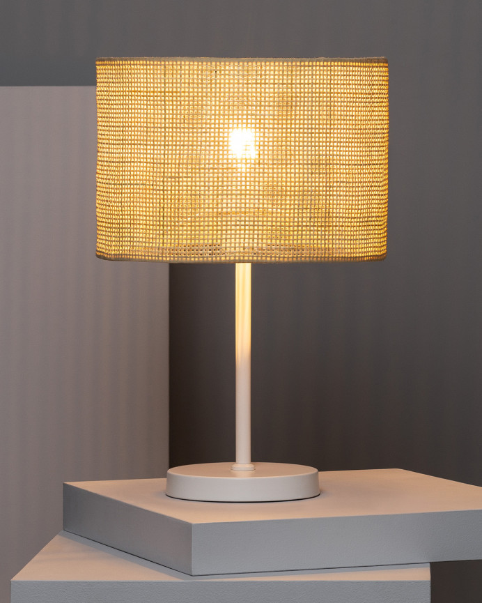 Lámpara de mesa elaborada con base metálica color blanco y pantalla de ratán.