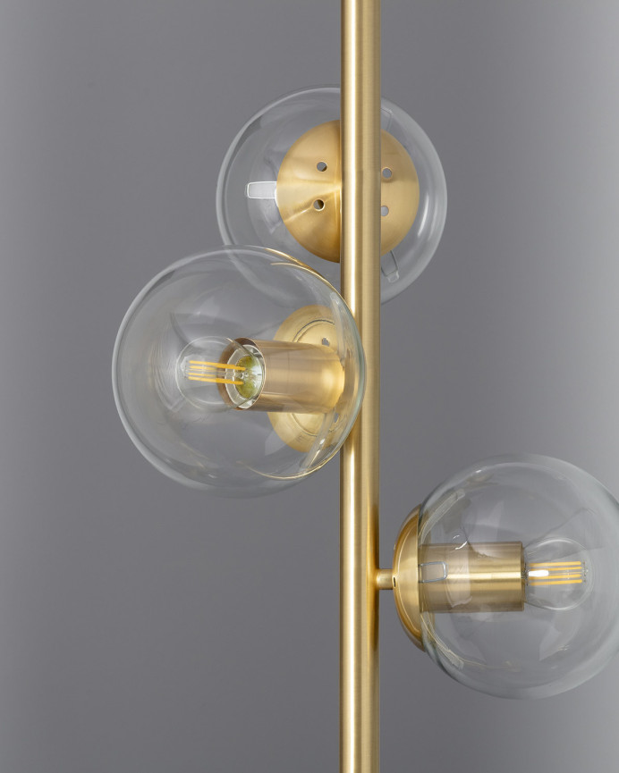 Lámpara de pie elaborada con una base de aluminio color dorado y tres esferas de cristal transparente.