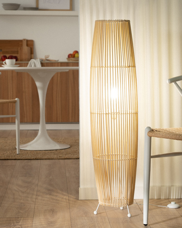 Lámpara de pie elaborada con base metálica color blanco y ramas de bambú unidas con un trenzado de fibras naturales.