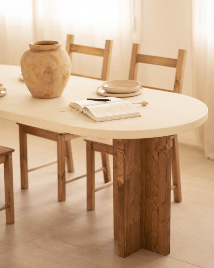 Mesa de comedor ovalada de microcemento en tono blanco roto con patas de madera tono roble oscuro de varias medidas