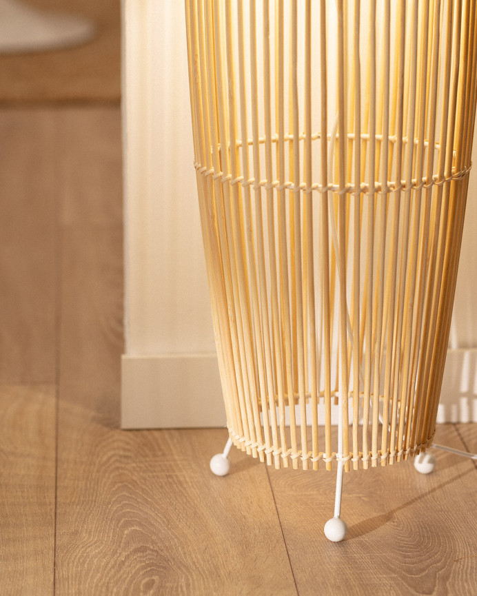 Lampadaire composé d'une base en métal blanc et de branches de bambou reliées par une tresse de fibres naturels.